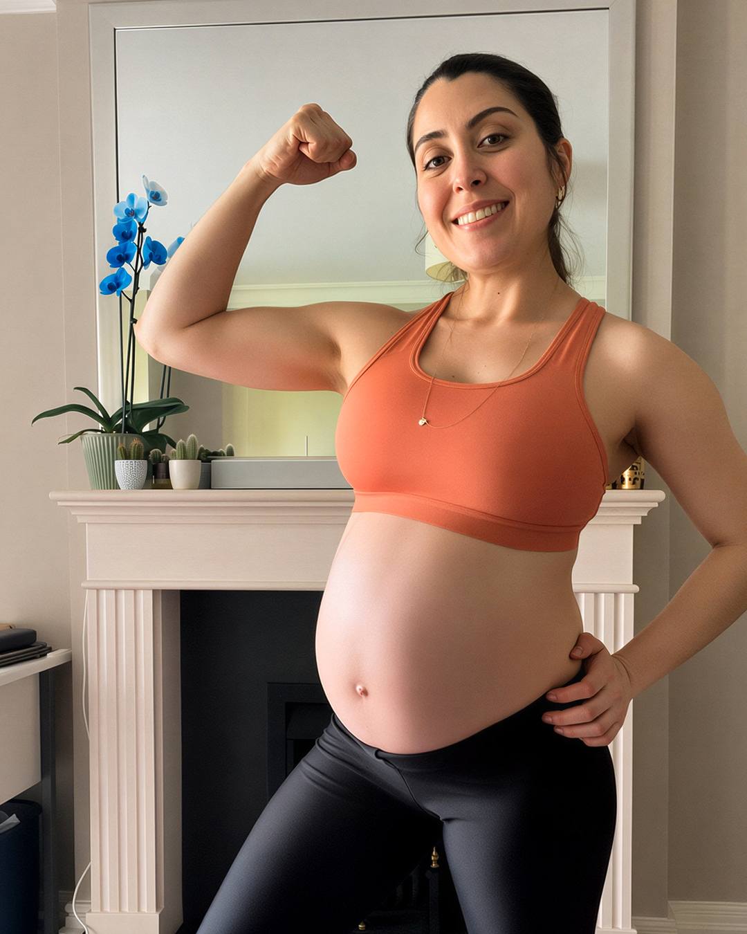 Rafaela Freitas smiling during pregnancy, wearing orange activewear and flexing her arm at home
